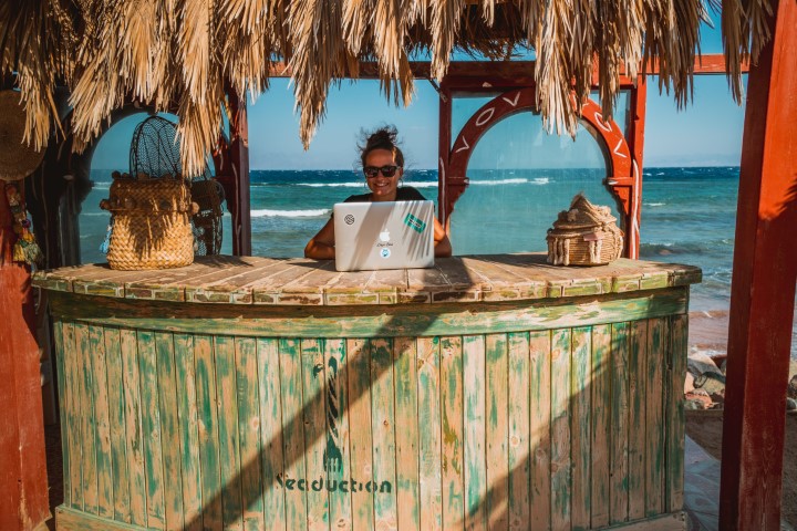 girl working on a laptop at a bar at the beach making money while traveling the world