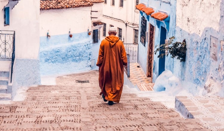 a man in a orange robe walking through the streets in Morocco's blue city