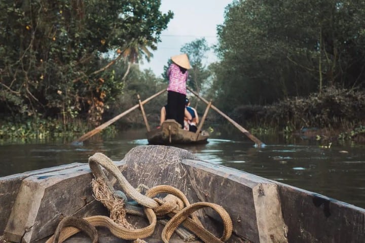 a lady standing up rowing a boat through the mekong delta