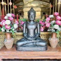 a bronze buddha in a temple surrounds by offerings of flowers